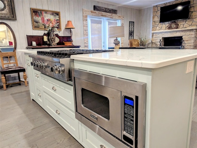 kitchen featuring light stone counters, light wood finished floors, stainless steel appliances, white cabinets, and wooden walls