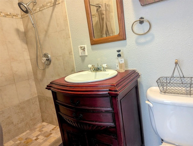 bathroom featuring toilet, a textured wall, a tile shower, and vanity