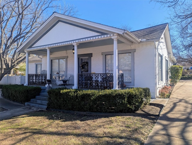 view of front of house featuring covered porch, a shingled roof, and brick siding