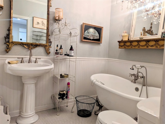 bathroom with a wainscoted wall, a soaking tub, a sink, and toilet