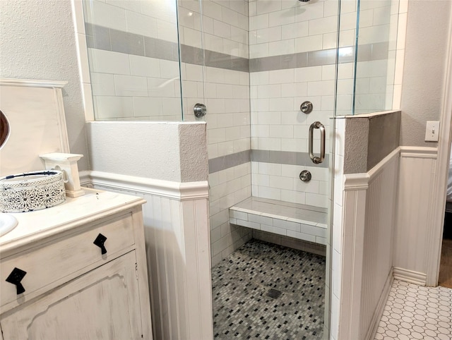 bathroom with a textured wall, a shower stall, vanity, and wainscoting