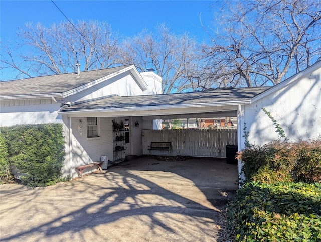 view of home's exterior with an attached carport, concrete driveway, fence, and a chimney