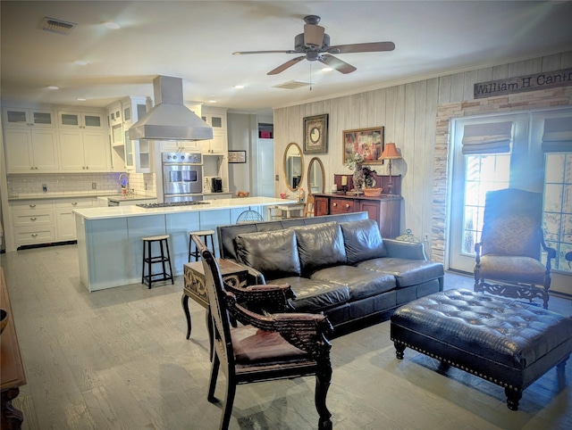 living room featuring ornamental molding, visible vents, light wood finished floors, and a ceiling fan