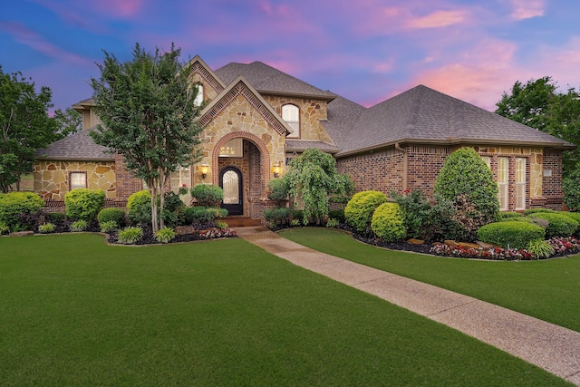 view of front facade with stone siding, brick siding, a front lawn, and a shingled roof