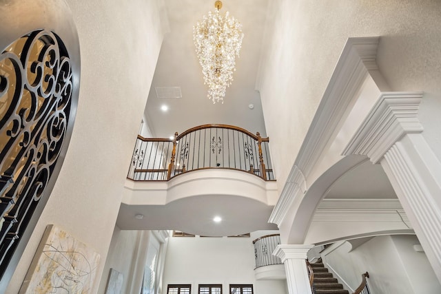 interior space with a chandelier, a textured wall, arched walkways, a high ceiling, and decorative columns