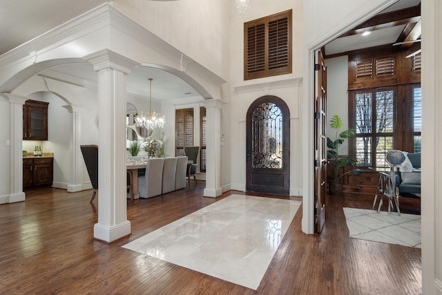 entryway with a towering ceiling, wood finished floors, decorative columns, and crown molding