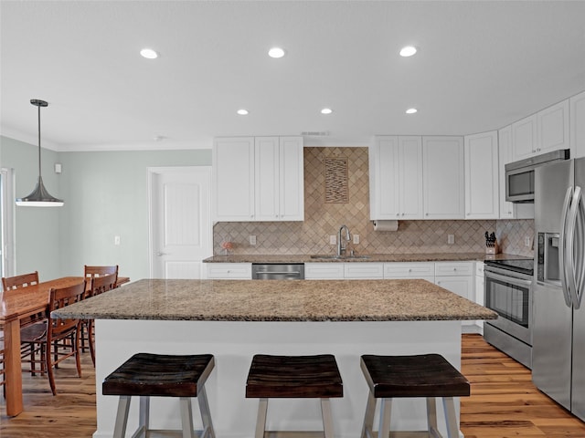 kitchen featuring stainless steel appliances, light wood-style flooring, white cabinets, a sink, and a kitchen breakfast bar