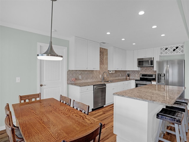 kitchen featuring stainless steel appliances, decorative backsplash, light wood-style floors, a sink, and a kitchen island