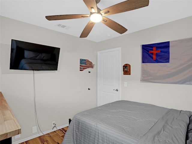 bedroom featuring a ceiling fan, visible vents, baseboards, and wood finished floors