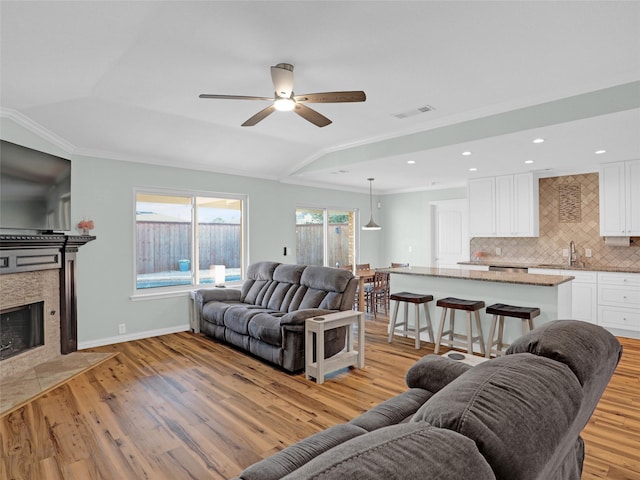 living area featuring lofted ceiling, a tile fireplace, visible vents, baseboards, and light wood-type flooring