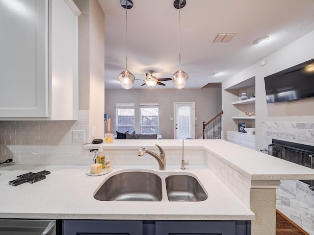 kitchen featuring a fireplace, visible vents, hanging light fixtures, backsplash, and a sink