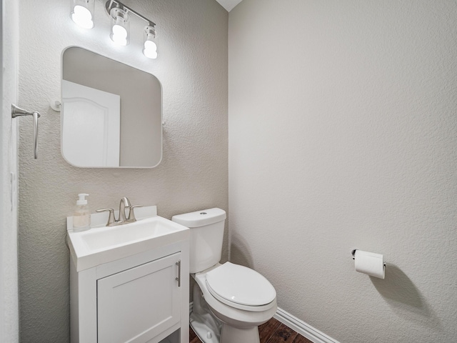 bathroom with toilet, a textured wall, wood finished floors, and vanity