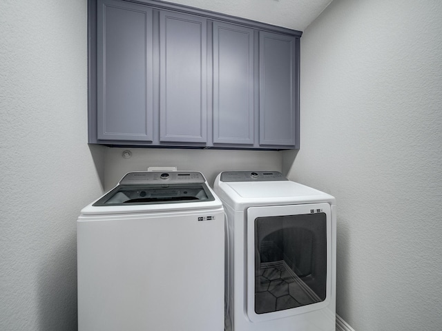 laundry room with washing machine and dryer, cabinet space, and a textured wall