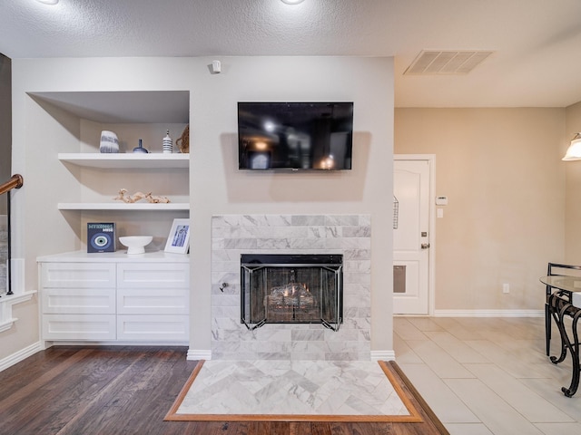 living room with built in features, baseboards, visible vents, a tile fireplace, and dark wood-type flooring