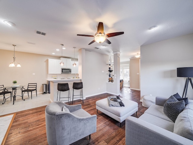 living area featuring ceiling fan with notable chandelier, light wood-type flooring, visible vents, and baseboards