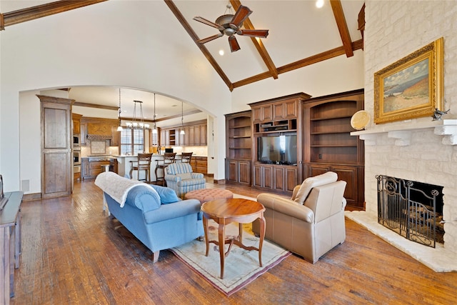 living room with arched walkways, dark wood-style flooring, a stone fireplace, high vaulted ceiling, and ceiling fan with notable chandelier