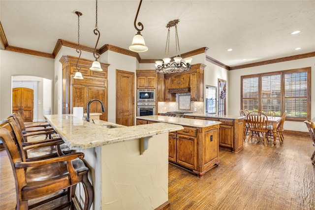 kitchen with arched walkways, stainless steel appliances, a sink, a large island, and brown cabinets