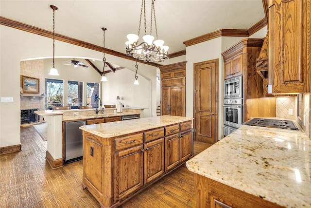 kitchen with a large fireplace, a sink, a kitchen island, appliances with stainless steel finishes, and brown cabinetry