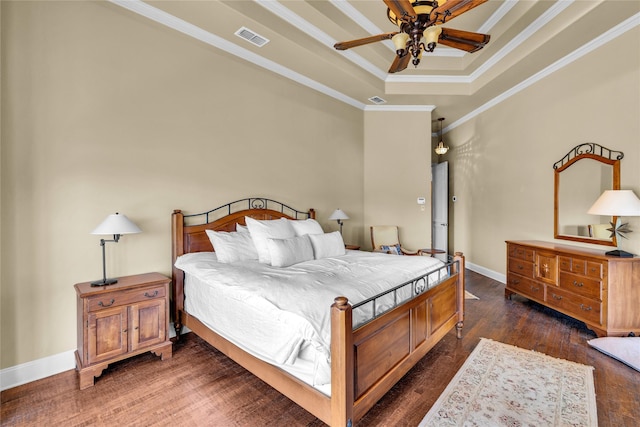 bedroom with baseboards, visible vents, wood finished floors, a tray ceiling, and crown molding