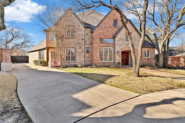 view of front facade with stone siding, brick siding, a front yard, and fence