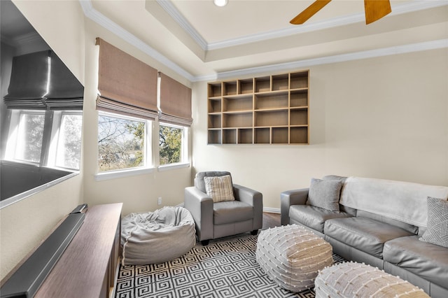 living room with a tray ceiling, a ceiling fan, and crown molding