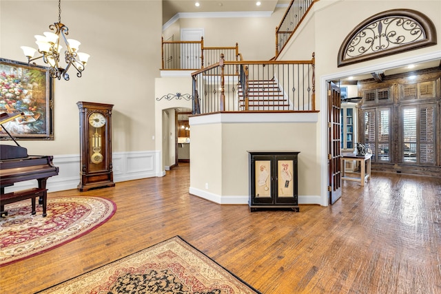 foyer featuring arched walkways, a towering ceiling, hardwood / wood-style floors, an inviting chandelier, and crown molding