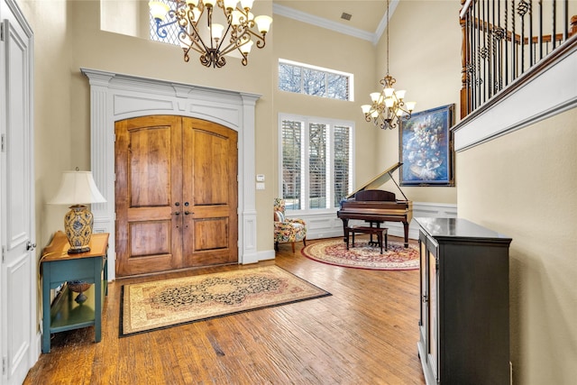 foyer entrance featuring ornamental molding, wood finished floors, a towering ceiling, and a notable chandelier