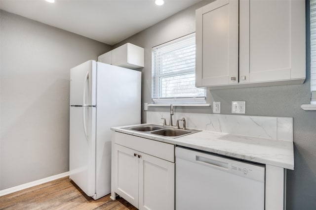 kitchen with white cabinetry, a sink, light wood-type flooring, white appliances, and baseboards