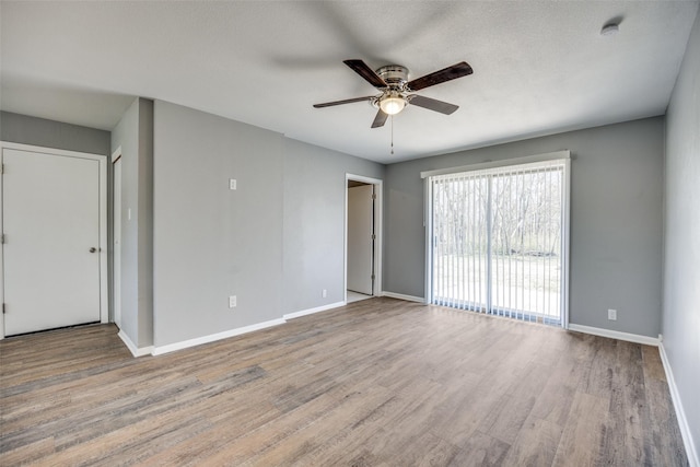 empty room with a textured ceiling, wood finished floors, a ceiling fan, and baseboards