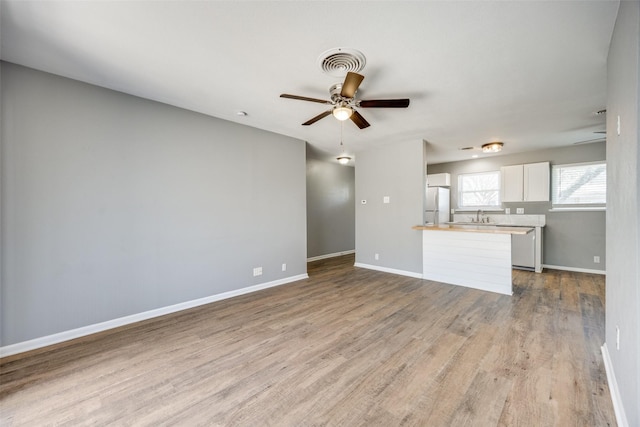 unfurnished living room featuring ceiling fan, visible vents, a sink, and wood finished floors