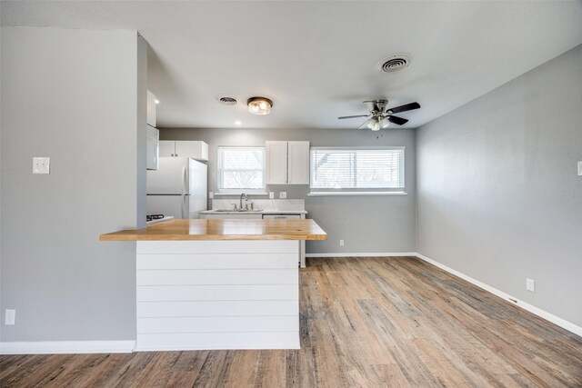 kitchen featuring butcher block counters, visible vents, freestanding refrigerator, a sink, and a peninsula