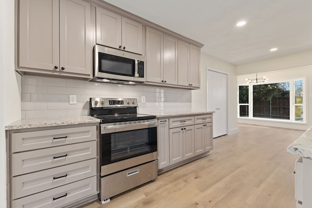 kitchen with stainless steel appliances, backsplash, light wood-style floors, light stone countertops, and a chandelier