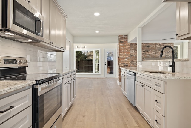 kitchen featuring decorative backsplash, light stone counters, stainless steel appliances, light wood-type flooring, and a sink