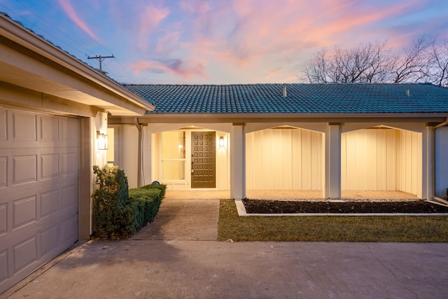 view of exterior entry with a tiled roof, an attached garage, and driveway