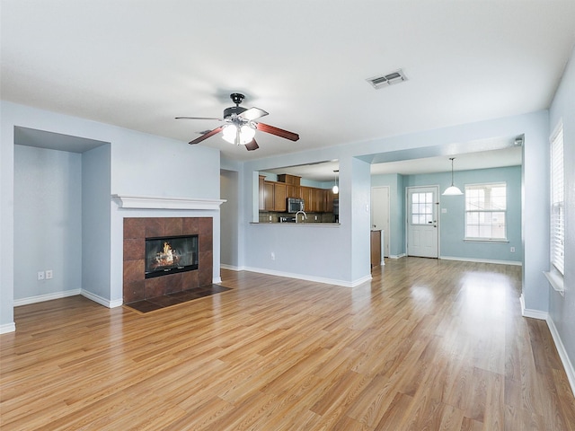 unfurnished living room featuring a fireplace, visible vents, light wood-style floors, a ceiling fan, and baseboards