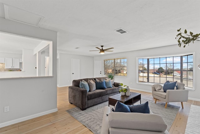 living area featuring light wood-style flooring, attic access, visible vents, and baseboards