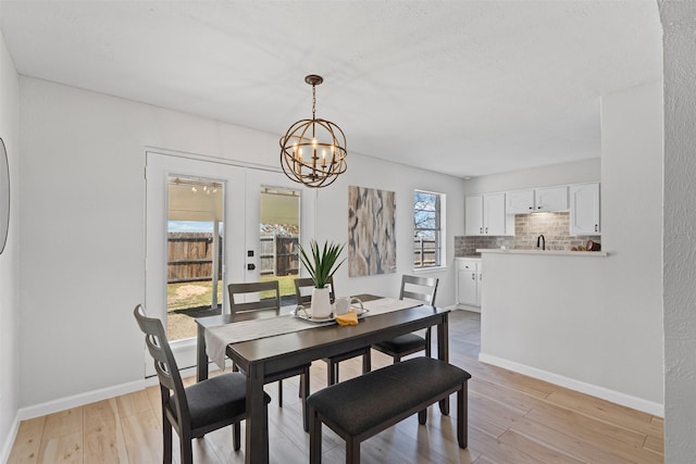 dining space with a textured ceiling, baseboards, light wood-style floors, french doors, and an inviting chandelier