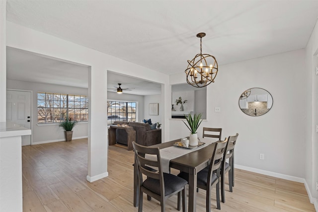 dining area with ceiling fan with notable chandelier, light wood-style flooring, and baseboards