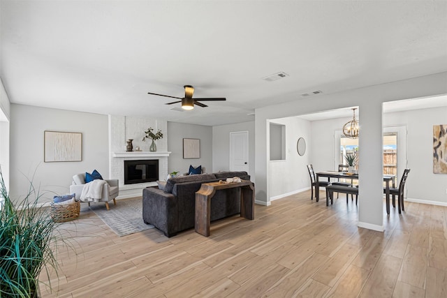 living room with a large fireplace, visible vents, light wood finished floors, and ceiling fan with notable chandelier