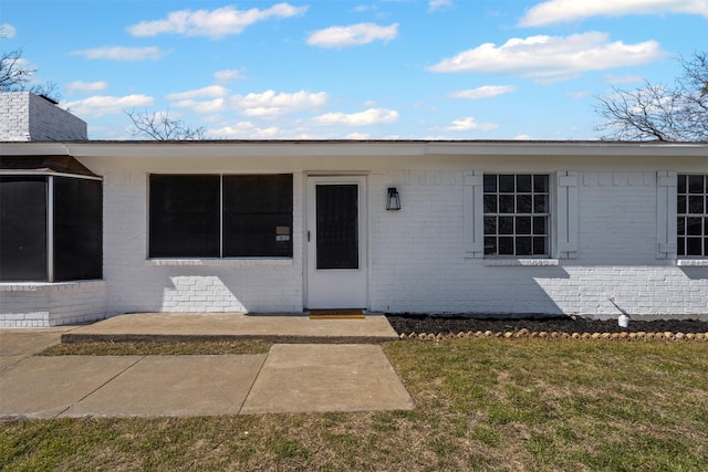 view of exterior entry with brick siding and a yard