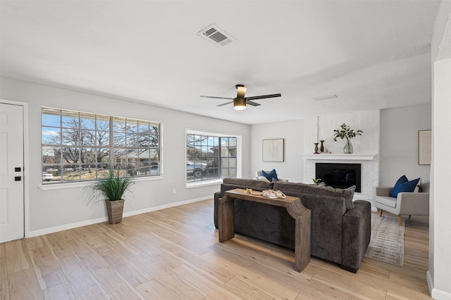 living area featuring baseboards, visible vents, a fireplace, and light wood finished floors