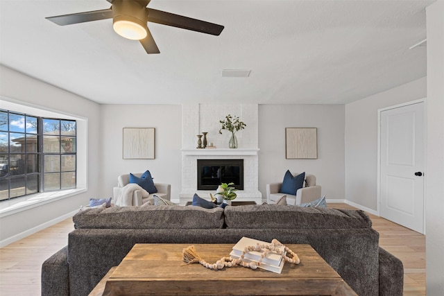 living room featuring light wood-style floors, a brick fireplace, baseboards, and a ceiling fan