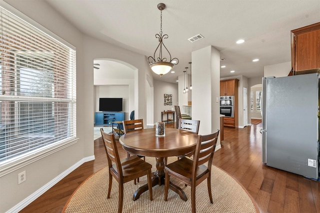 dining room featuring dark wood-style floors, baseboards, visible vents, and arched walkways