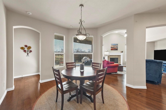 dining room with baseboards, arched walkways, a ceiling fan, a tile fireplace, and hardwood / wood-style flooring