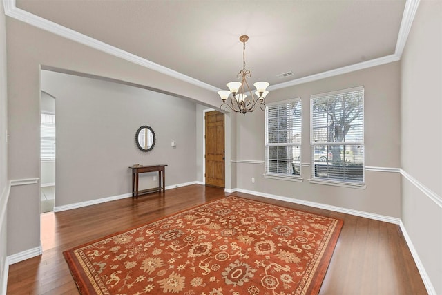 empty room with visible vents, ornamental molding, wood finished floors, a chandelier, and baseboards