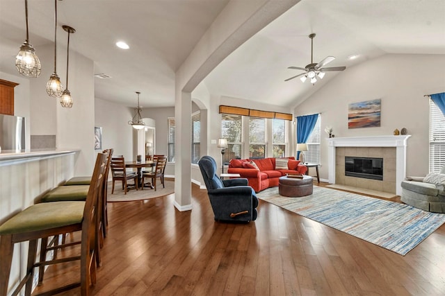 living room featuring dark wood-style floors, vaulted ceiling, a tiled fireplace, and arched walkways