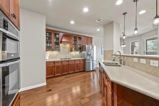 kitchen featuring stainless steel appliances, premium range hood, a sink, visible vents, and light wood-type flooring