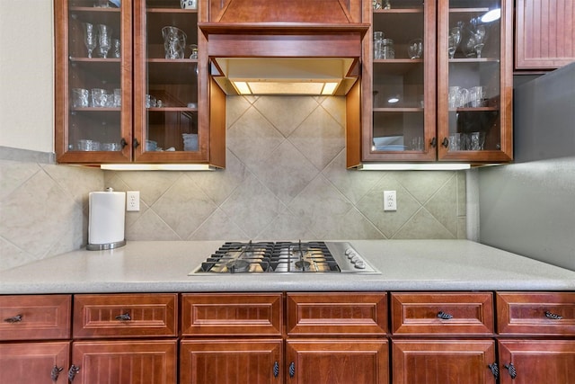 kitchen with glass insert cabinets, reddish brown cabinets, and stainless steel gas cooktop