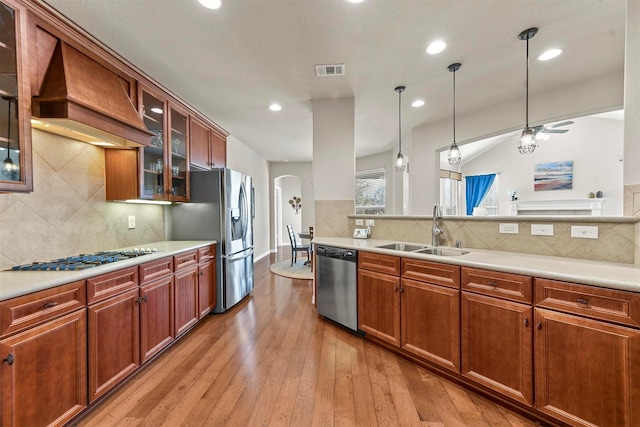 kitchen with light wood finished floors, stainless steel appliances, visible vents, a sink, and premium range hood