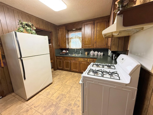 kitchen featuring white appliances, dark countertops, a textured ceiling, under cabinet range hood, and a sink